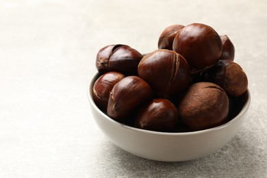 Photo of Fresh edible sweet chestnuts in bowl on grey table. Space for text