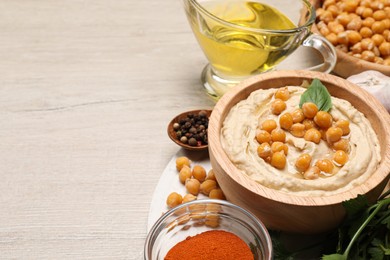 Photo of Delicious hummus with chickpeas and different ingredients on white wooden table. Space for text