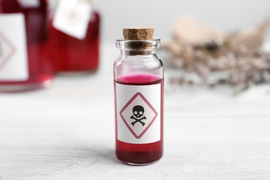 Photo of Vial of poison with warning sign on white wooden table, closeup