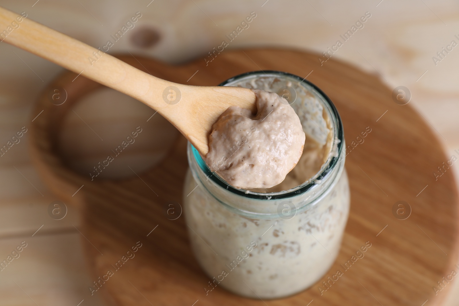 Photo of Taking sourdough starter with spoon at table, closeup