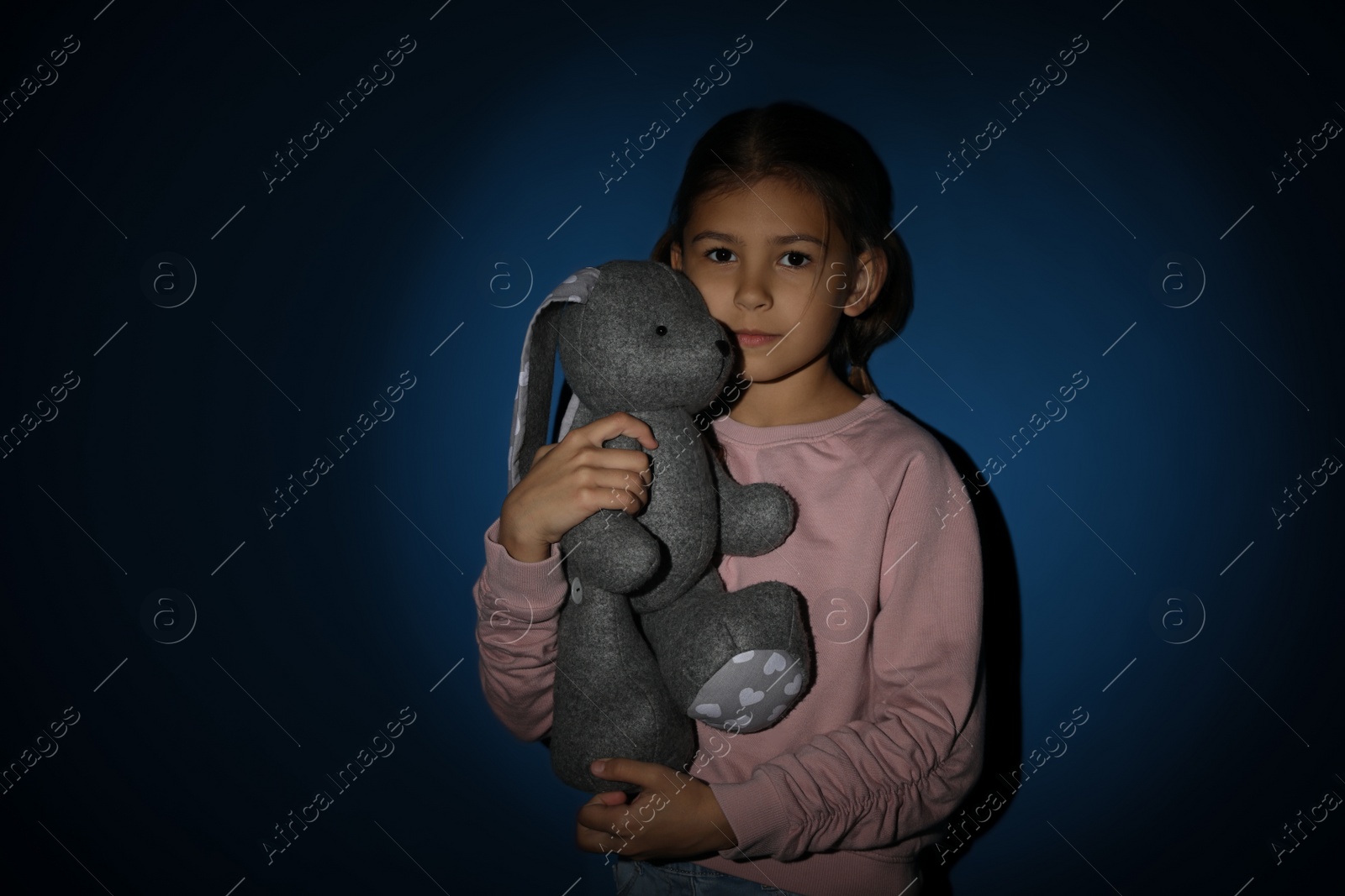 Photo of Sad little girl with toy near blue wall. Domestic violence concept