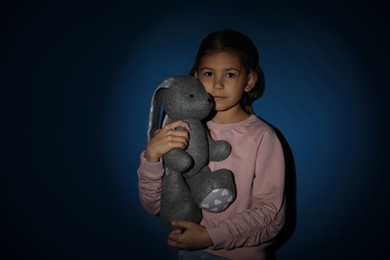 Sad little girl with toy near blue wall. Domestic violence concept