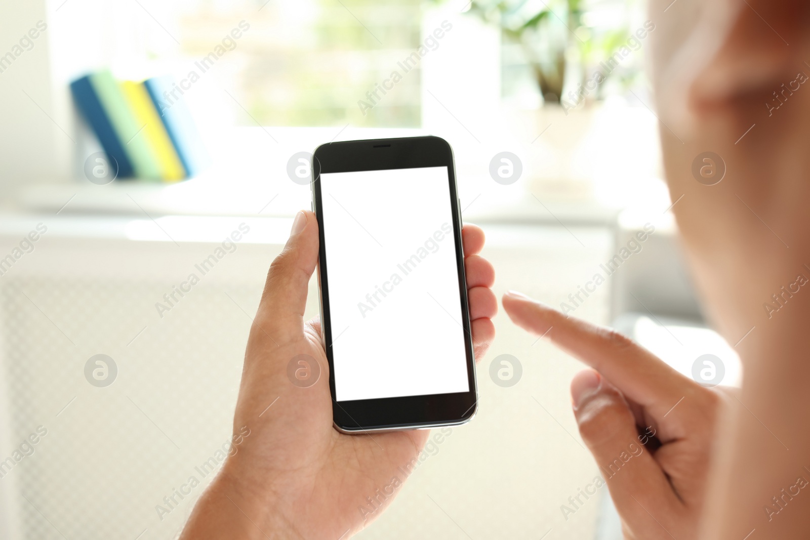 Photo of Young man holding mobile phone with blank screen on blurred background, closeup