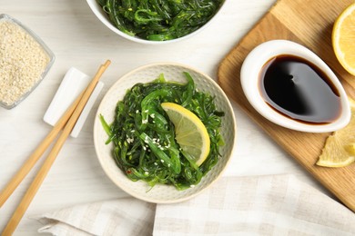 Photo of Japanese seaweed salad with lemon slice served on white wooden table, flat lay