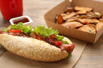 Photo of Hot dog, potato wedges and ketchup on wooden table, closeup. Fast food