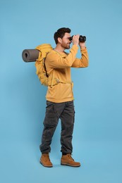 Photo of Man with backpack looking through binoculars on light blue background. Active tourism