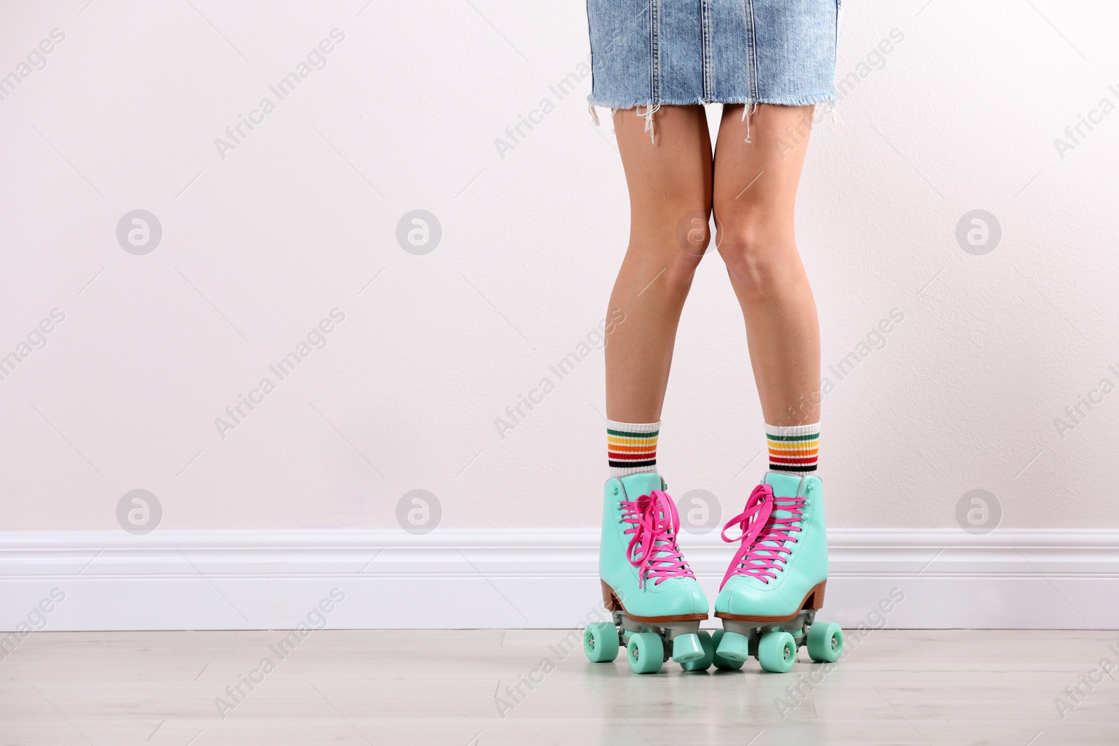 Photo of Young woman with retro roller skates near white wall, closeup. Space for text