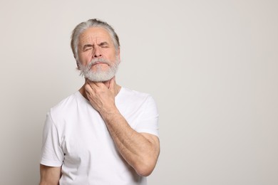 Photo of Senior man suffering from sore throat on white background, space for text. Cold symptoms