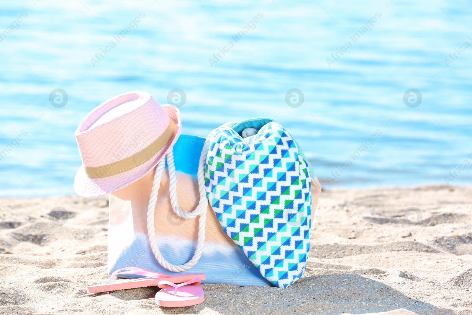 Photo of Bag, towel, hat and flip flops on sand near sea. Beach object