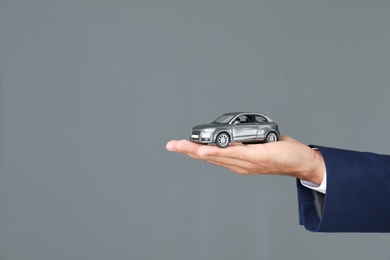 Photo of Insurance agent holding toy car on gray background, closeup