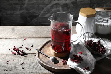 Freshly brewed hibiscus tea in teapot and dry flower petals on wooden table. Space for text