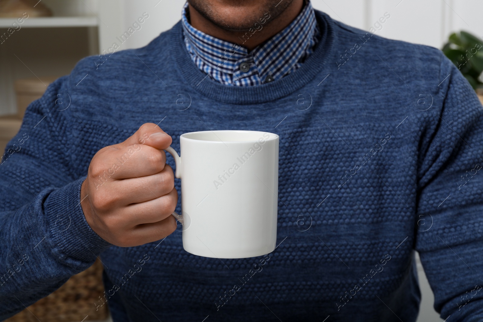 Photo of Man holding white mug indoors, closeup. Mockup for design