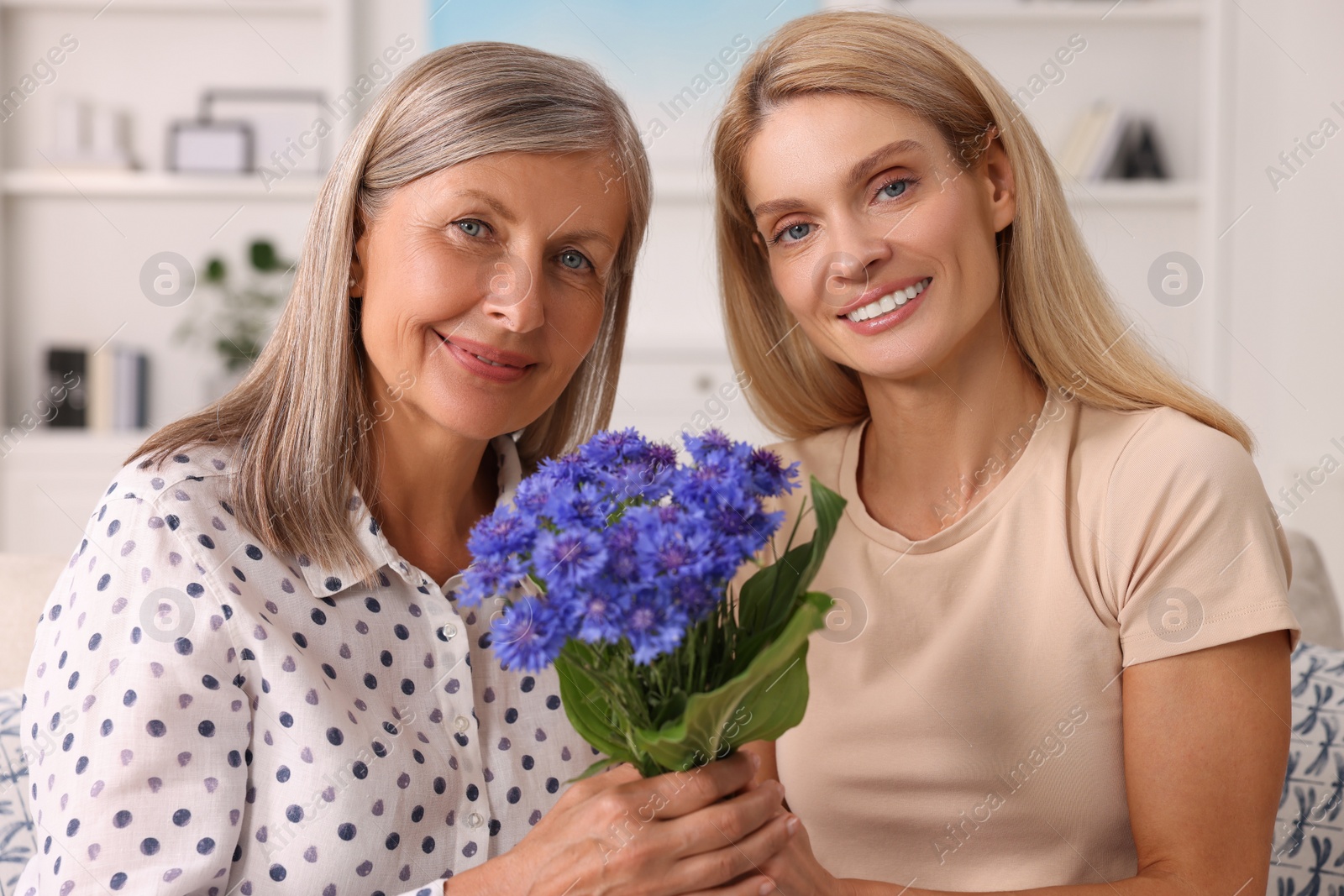 Photo of Happy mature mother and her daughter with beautiful cornflowers at home