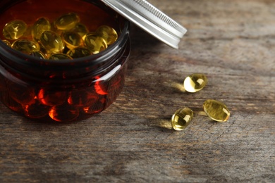 Jar with cod liver oil pills on wooden background, closeup