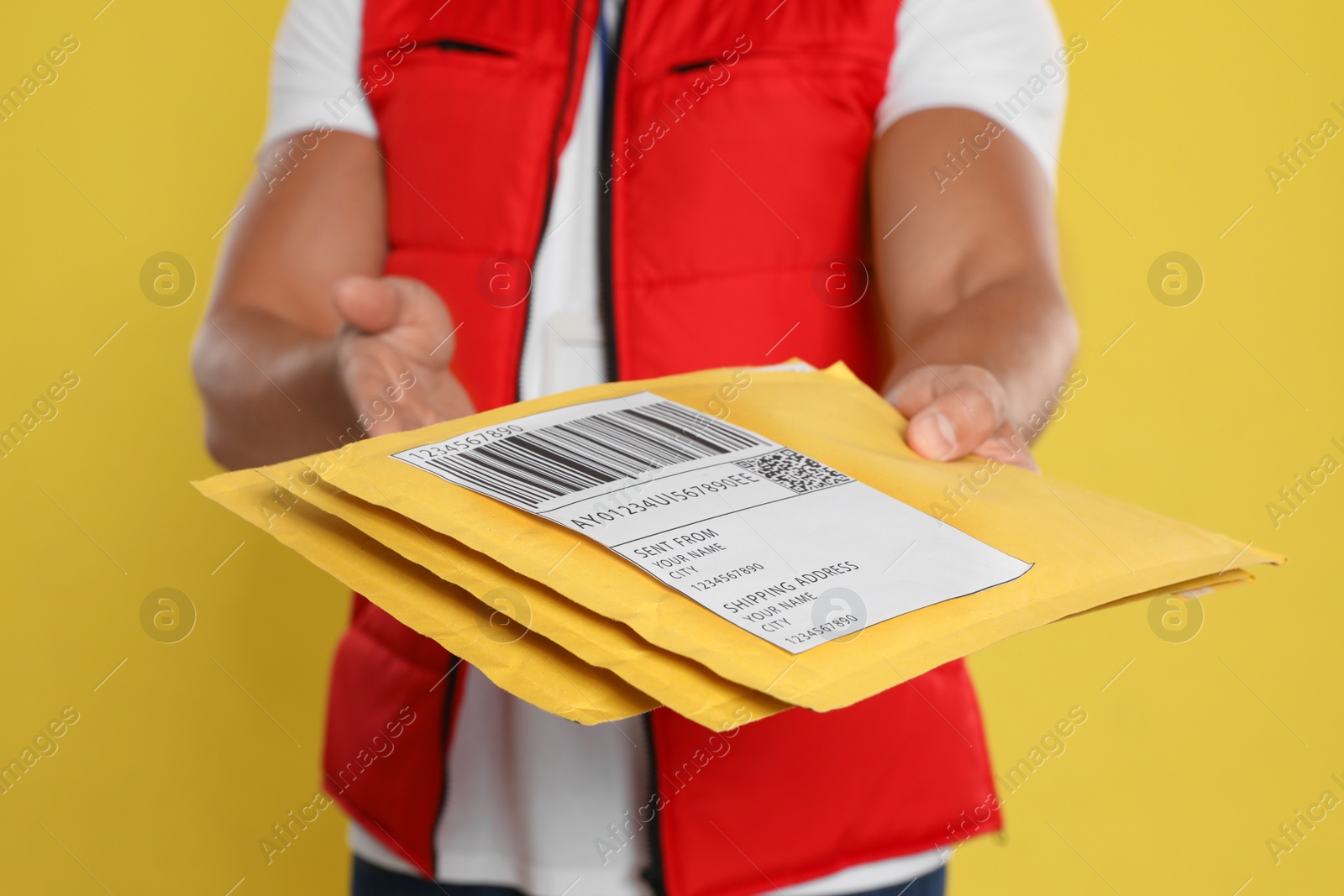 Photo of Young courier with envelopes on yellow background, closeup
