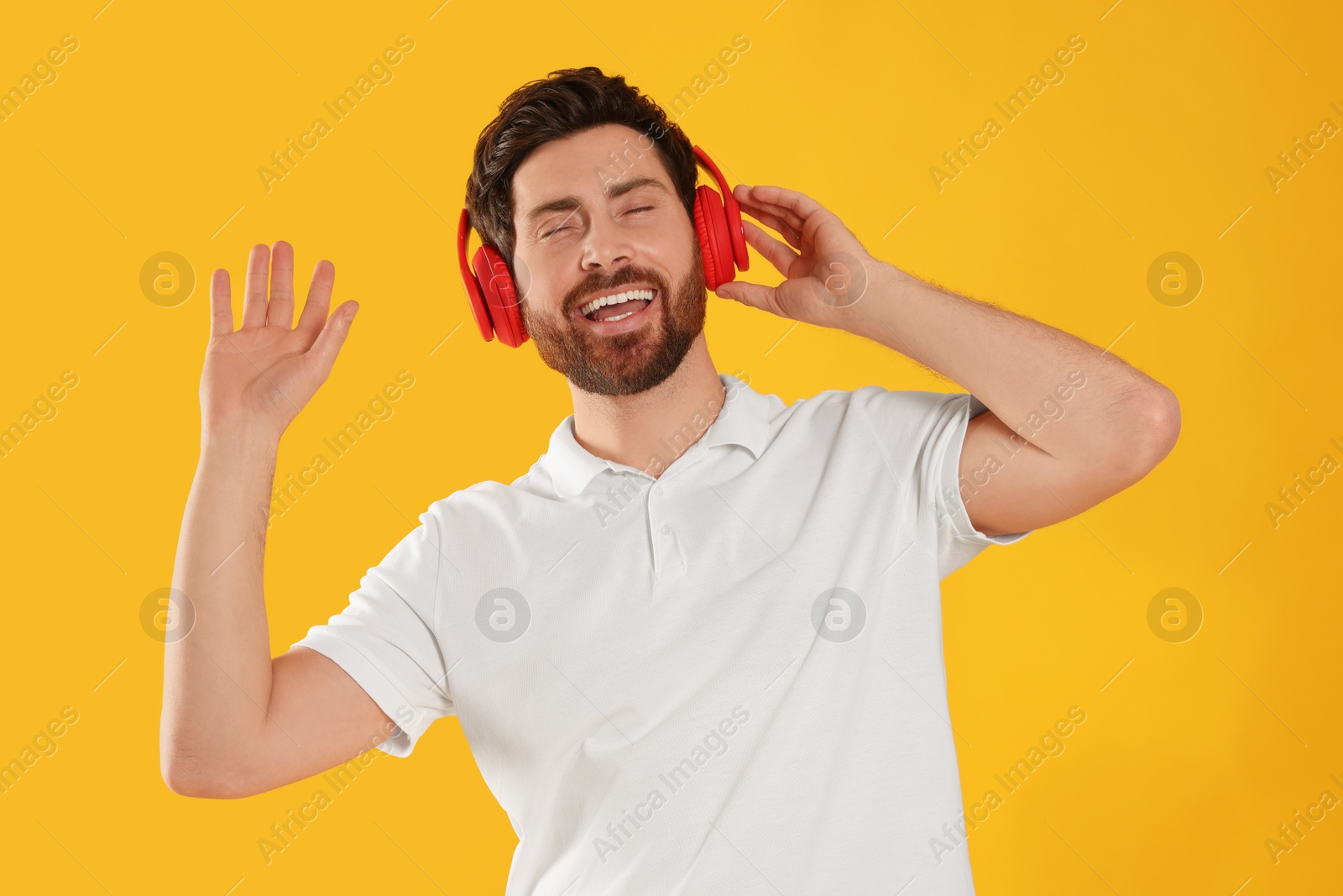 Photo of Happy man listening music with headphones on yellow background