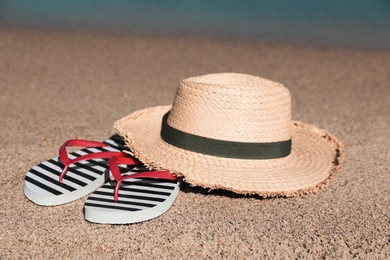 Photo of Striped flip flops and straw hat on sandy beach near sea