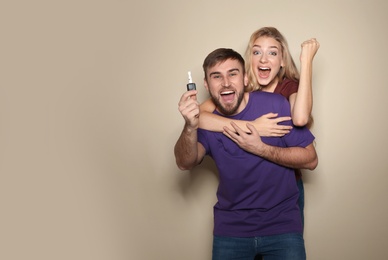 Happy young couple with car key on color background, space for text