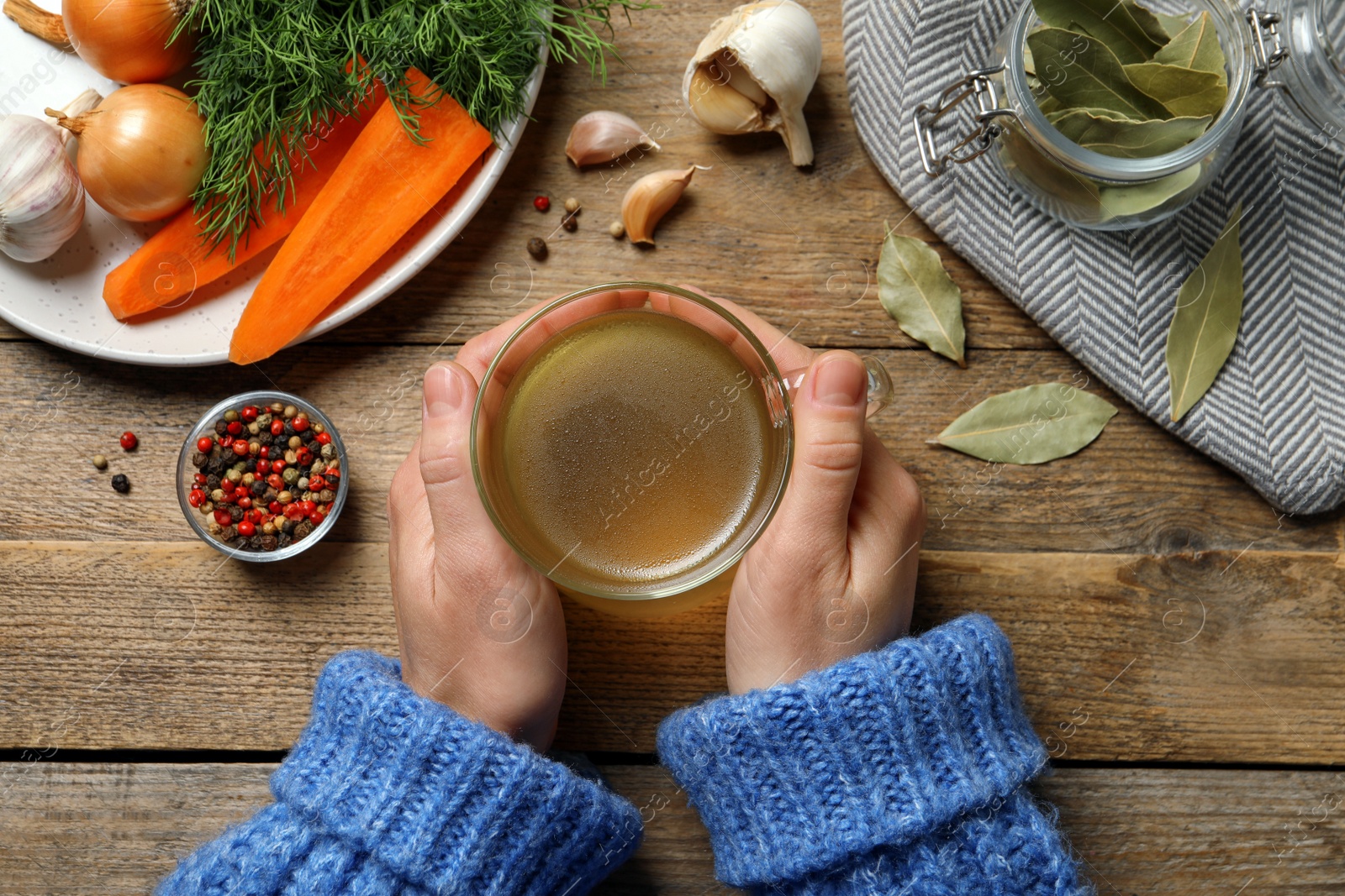 Photo of Woman with glass cup of hot delicious bouillon at wooden table, top view