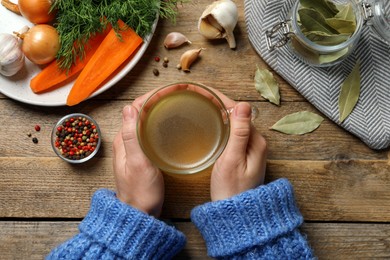 Photo of Woman with glass cup of hot delicious bouillon at wooden table, top view