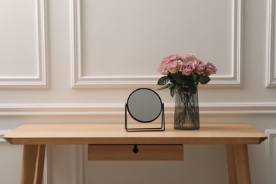 Mirror and vase with pink roses on wooden dressing table in makeup room, space for text