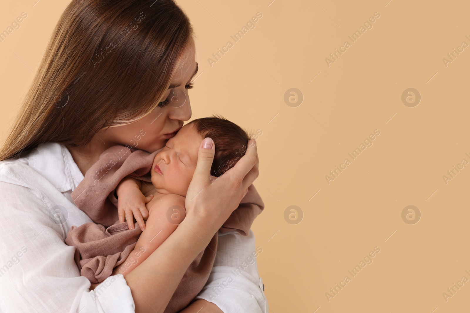 Photo of Mother kissing her cute newborn baby on beige background. Space for text