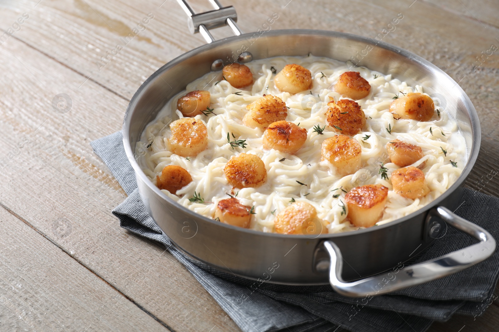 Photo of Delicious scallop pasta in pan on wooden table, closeup