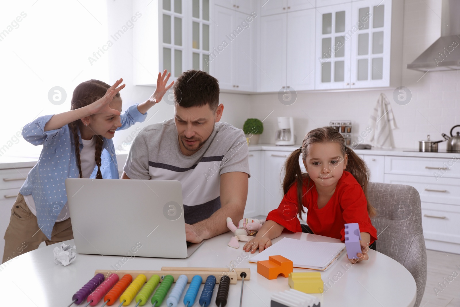 Photo of Children disturbing stressed man in kitchen. Working from home during quarantine