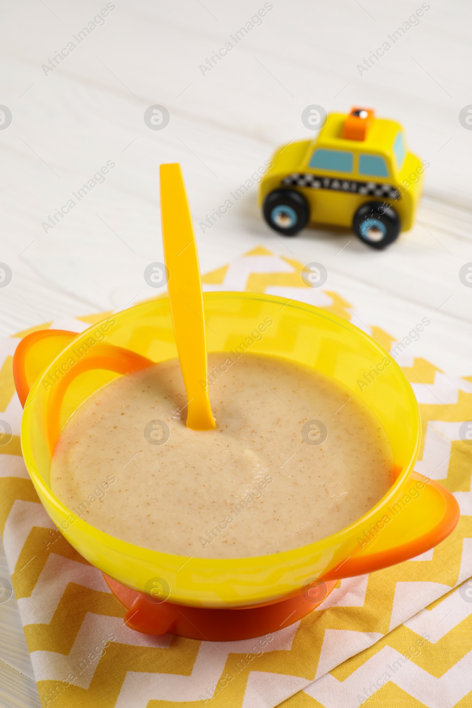 Photo of Baby food. Puree, spoon and toy on white wooden table