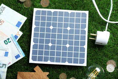Photo of Flat lay composition with solar panel, house model and money on green grass