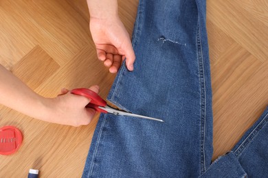 Photo of Woman cutting jeans with scissors at wooden table, top view
