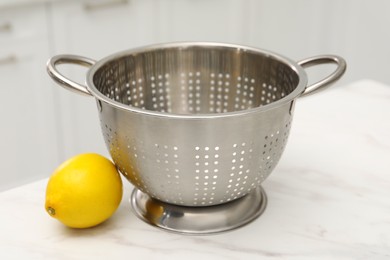 Empty colander and fresh lemon on white marble table