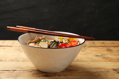 Photo of Bowl of delicious ramen and chopsticks on wooden table. Noodle soup