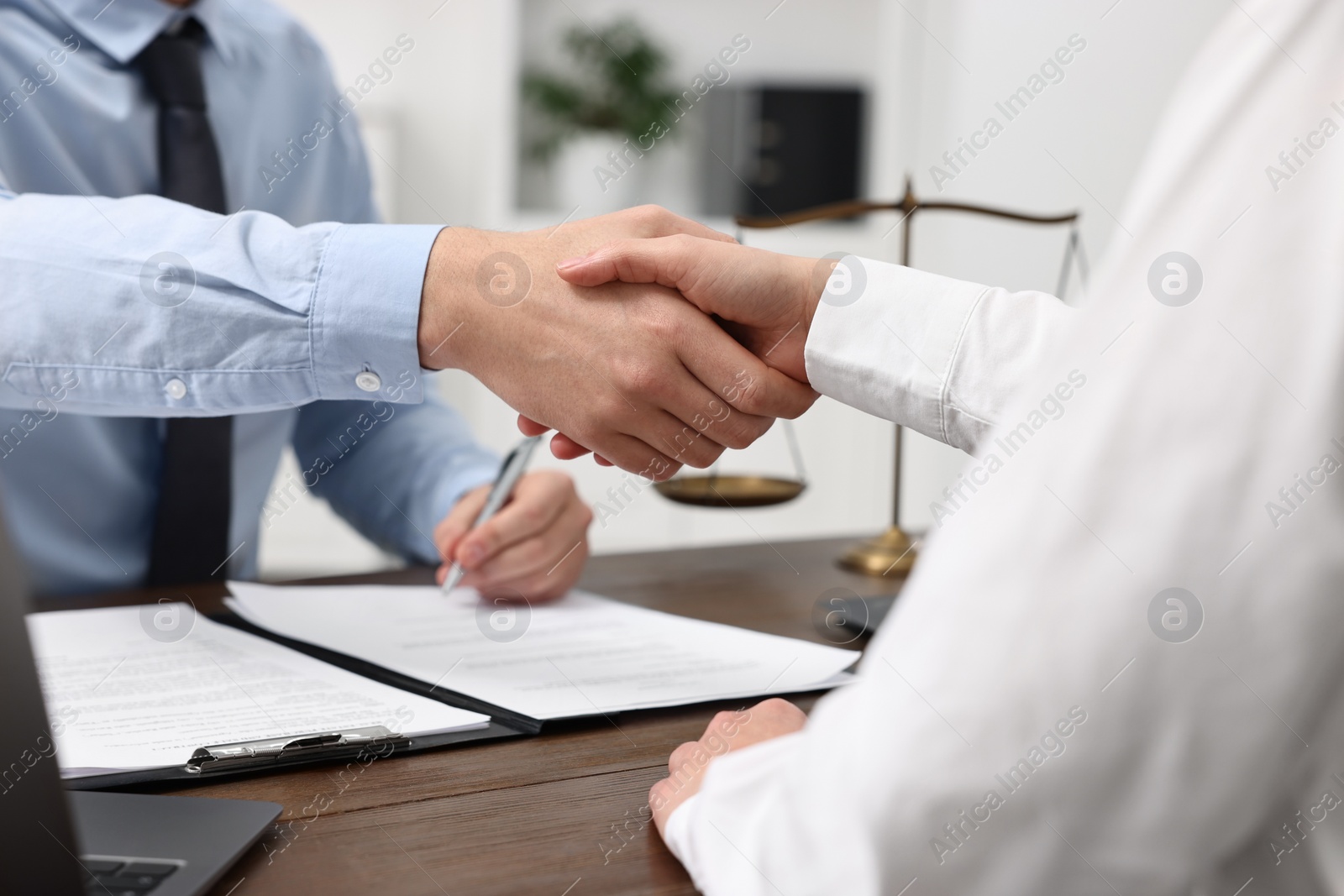 Photo of Lawyers shaking hands at wooden table in office, closeup