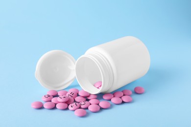 Photo of Pink antidepressants with emoticons and medical jar on light blue background