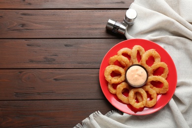 Plate with fried onion rings and sauce on table, top view