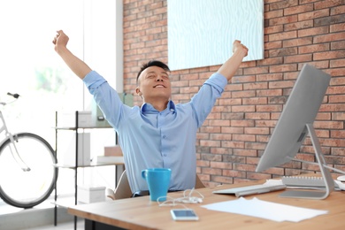 Photo of Happy young businessman stretching at workplace. Enjoying peaceful moment