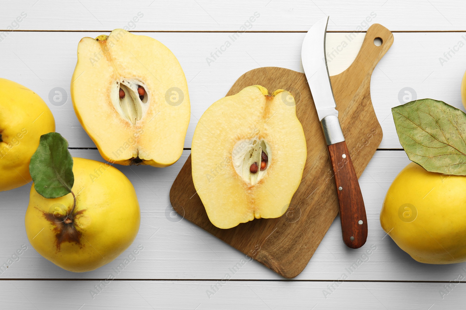 Photo of Tasty ripe quince fruits and knife on white wooden table, flat lay