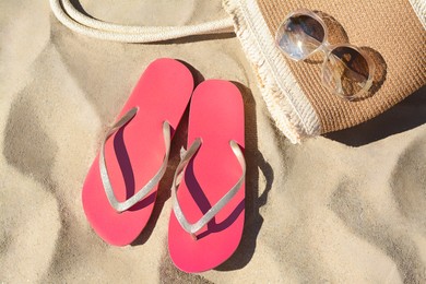 Photo of Pink flip flops, sunglasses and straw bag on sand, flat lay. Beach accessories