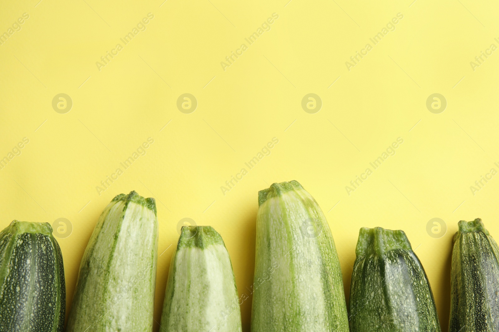 Photo of Fresh ripe green zucchinis on yellow background, flat lay. Space for text