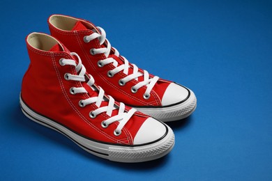 Photo of Pair of new stylish red sneakers on blue background