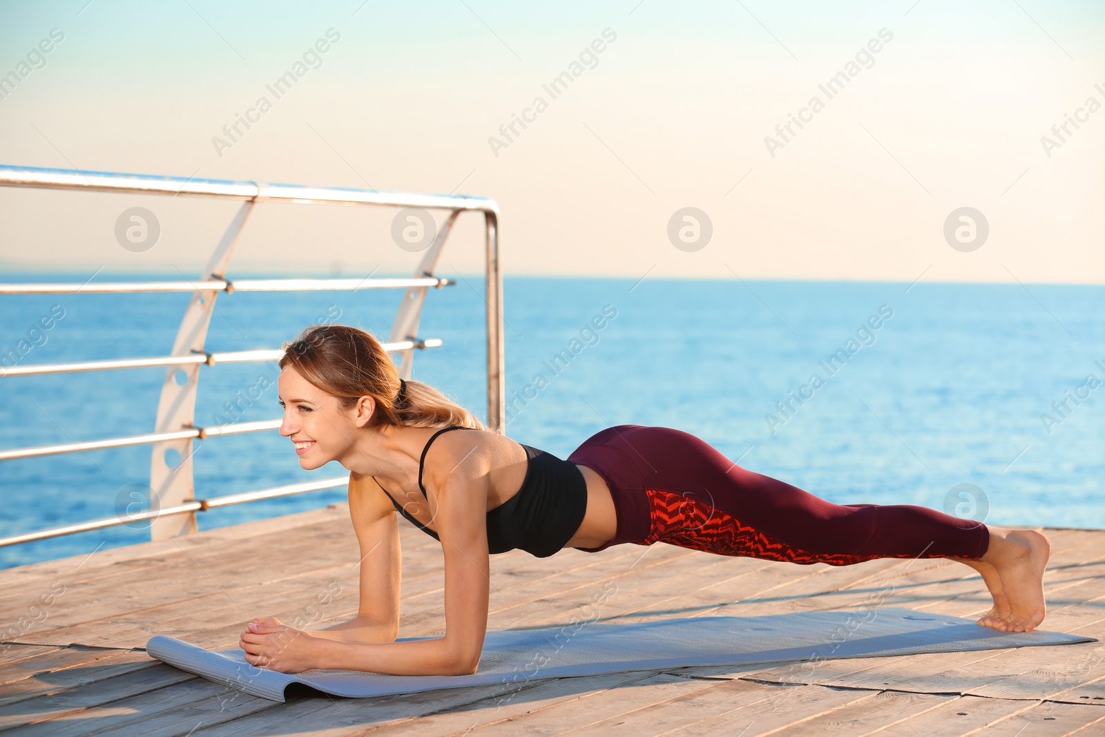 Photo of Young woman doing yoga exercises on pier in morning
