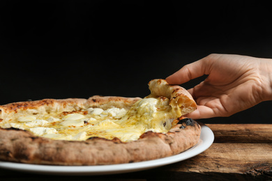 Woman taking slice of tasty cheese pizza at wooden table, closeup