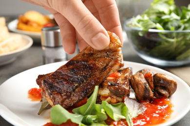 Woman with tasty grilled ribs at table, closeup