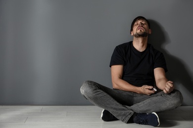 Photo of Male drug addict with syringe sitting near grey wall. Space for text