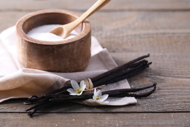 Photo of Vanilla pods, sugar in bowl and flowers on wooden table, closeup