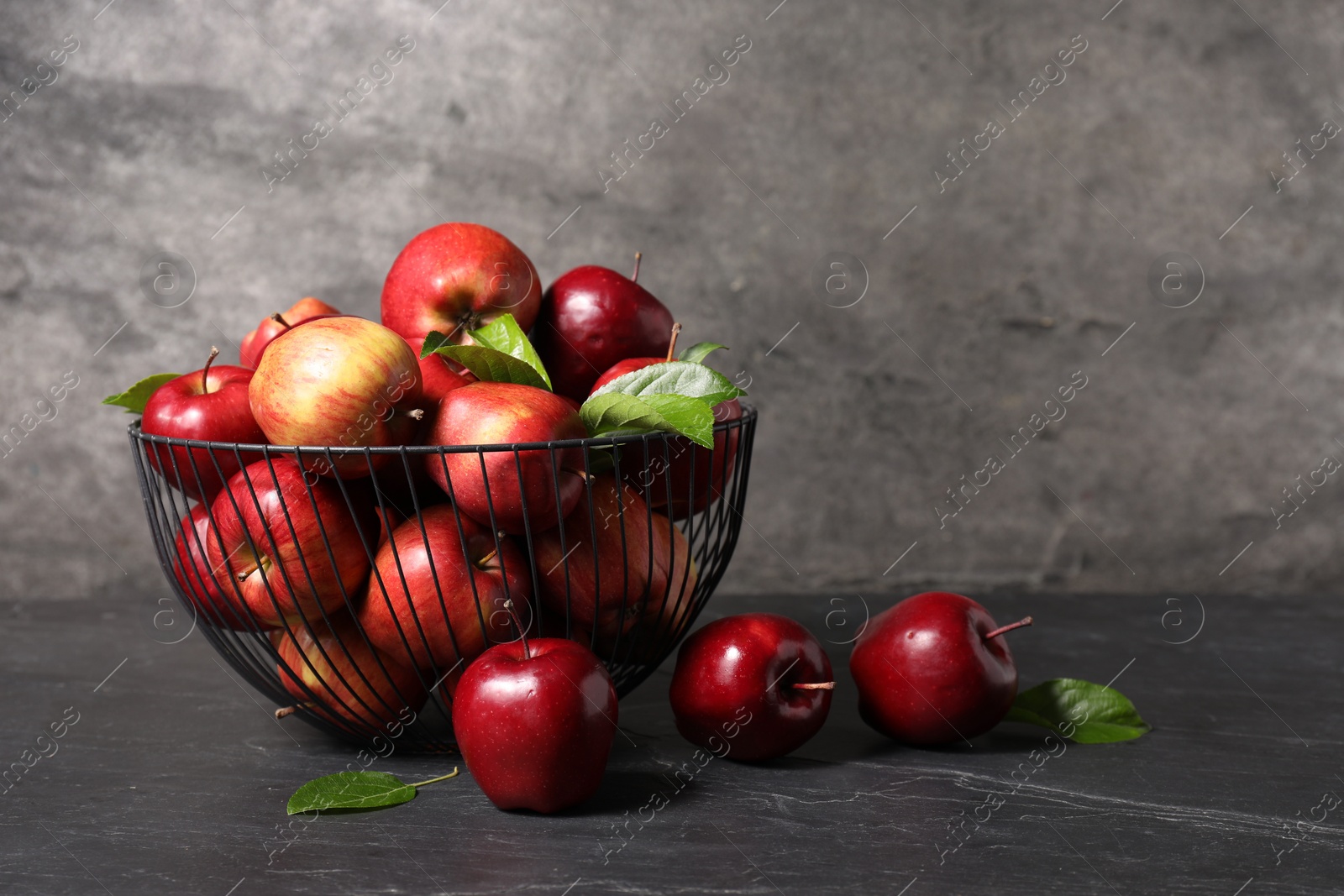 Photo of Fresh red apples and leaves on dark grey table. Space for text