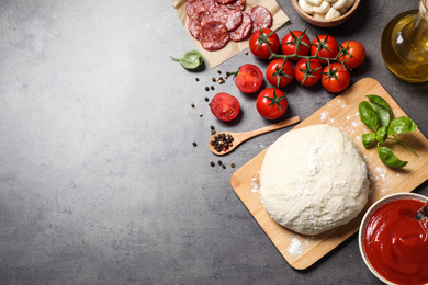 Photo of Flat lay composition with dough and ingredients on grey table, space for text. Pepperoni pizza recipe