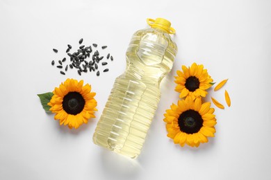 Bottle of cooking oil, sunflowers and seeds on white table, flat lay