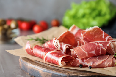 Photo of Slices of tasty prosciutto on grey table, closeup